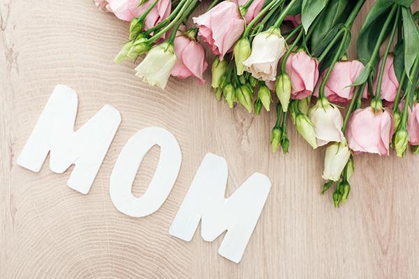 Bouquet of pink and white flowers with white wooden letters spelling MOM on wood surface