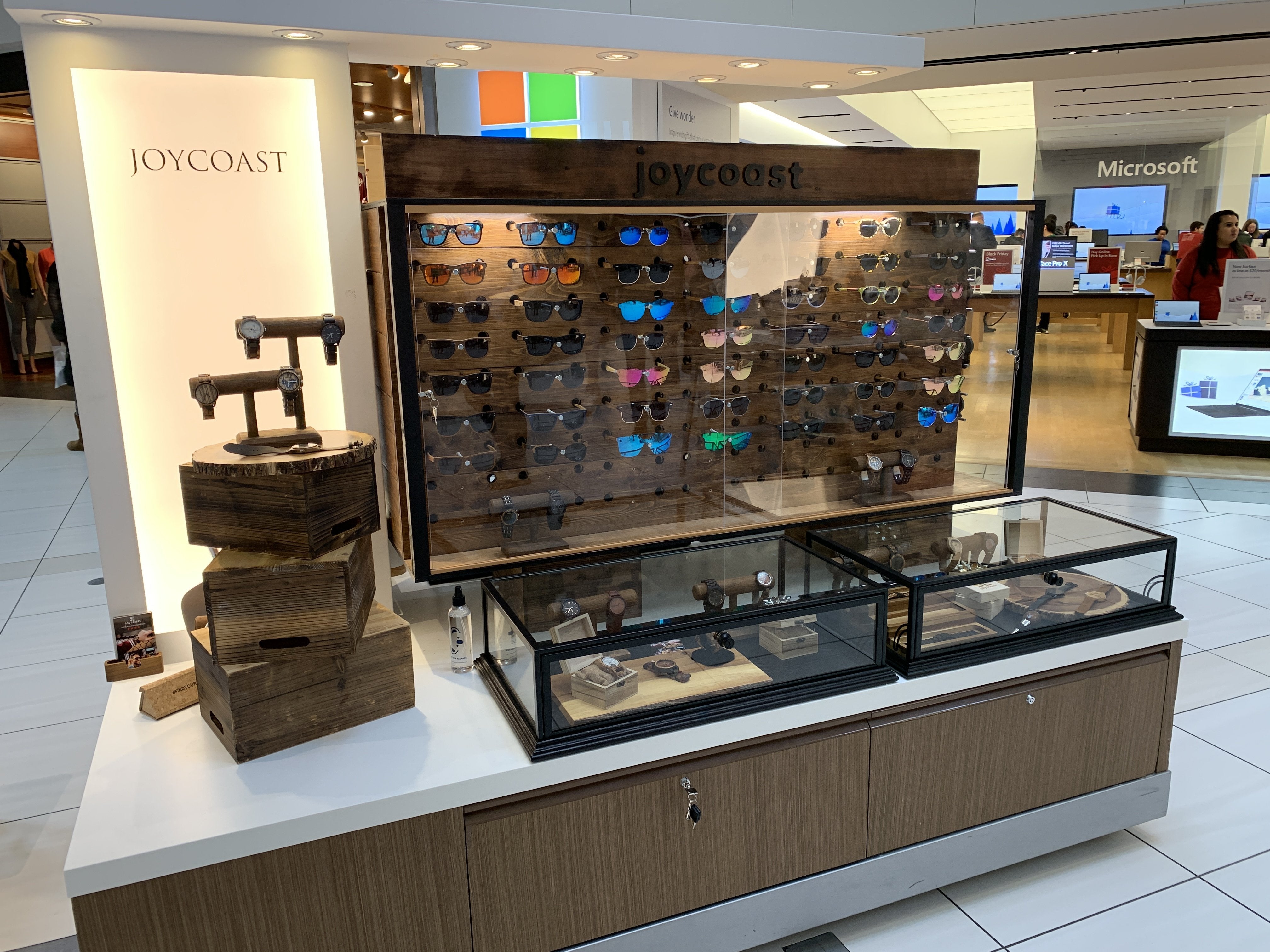 Joycoast wooden watches and sunglasses display in mall with wooden crates and glass cases