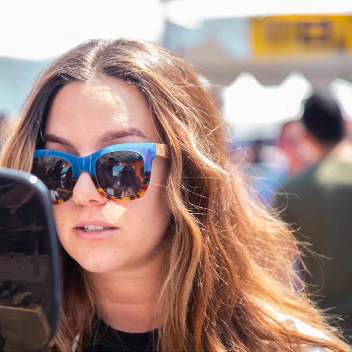 Woman with long hair wearing blue and tortoiseshell polarized wooden sunglasses by Joycoast at outdoor event
