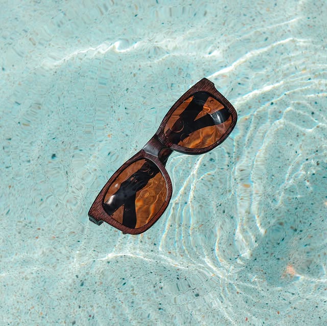 Joycoast wooden sunglasses with brown lenses floating in clear blue water with sunlight reflections