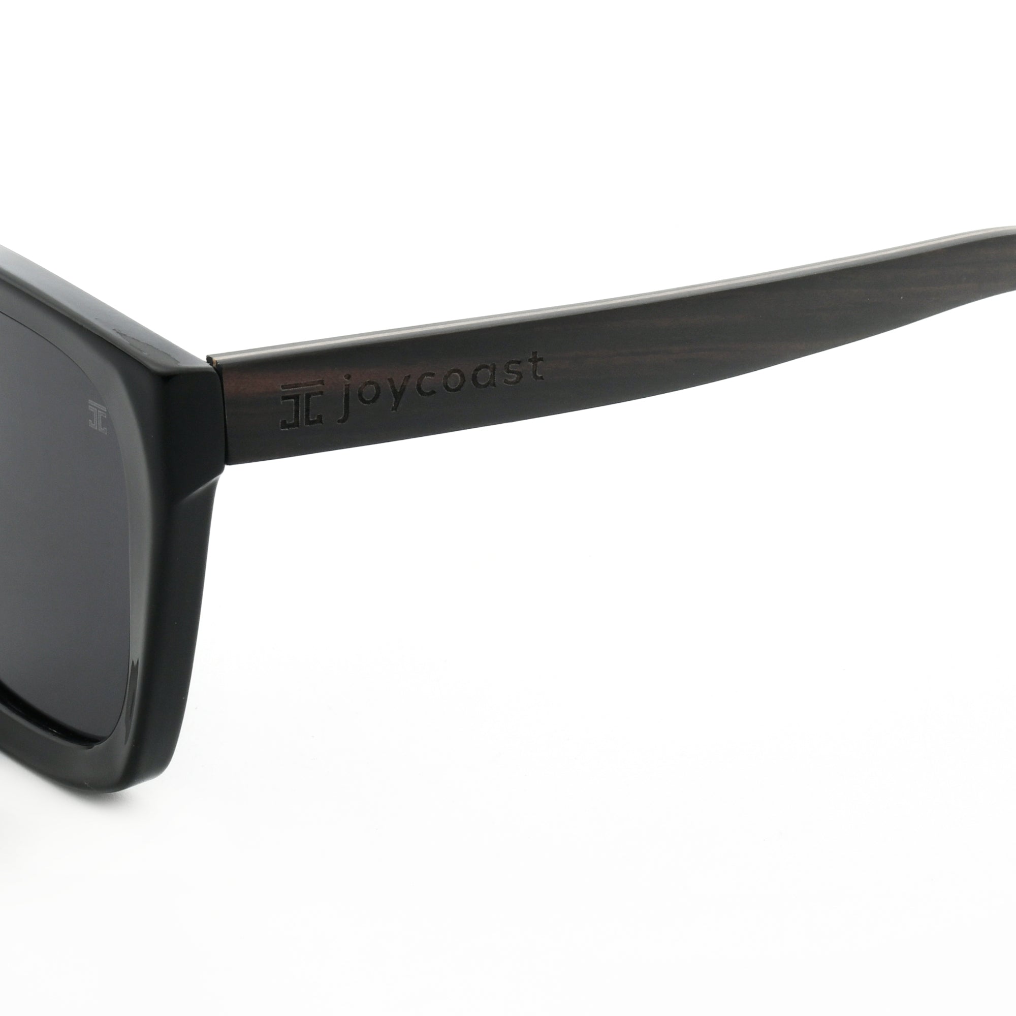 Close-up of black sunglasses frame with "Joycoast" logo engraved near the dark lens.