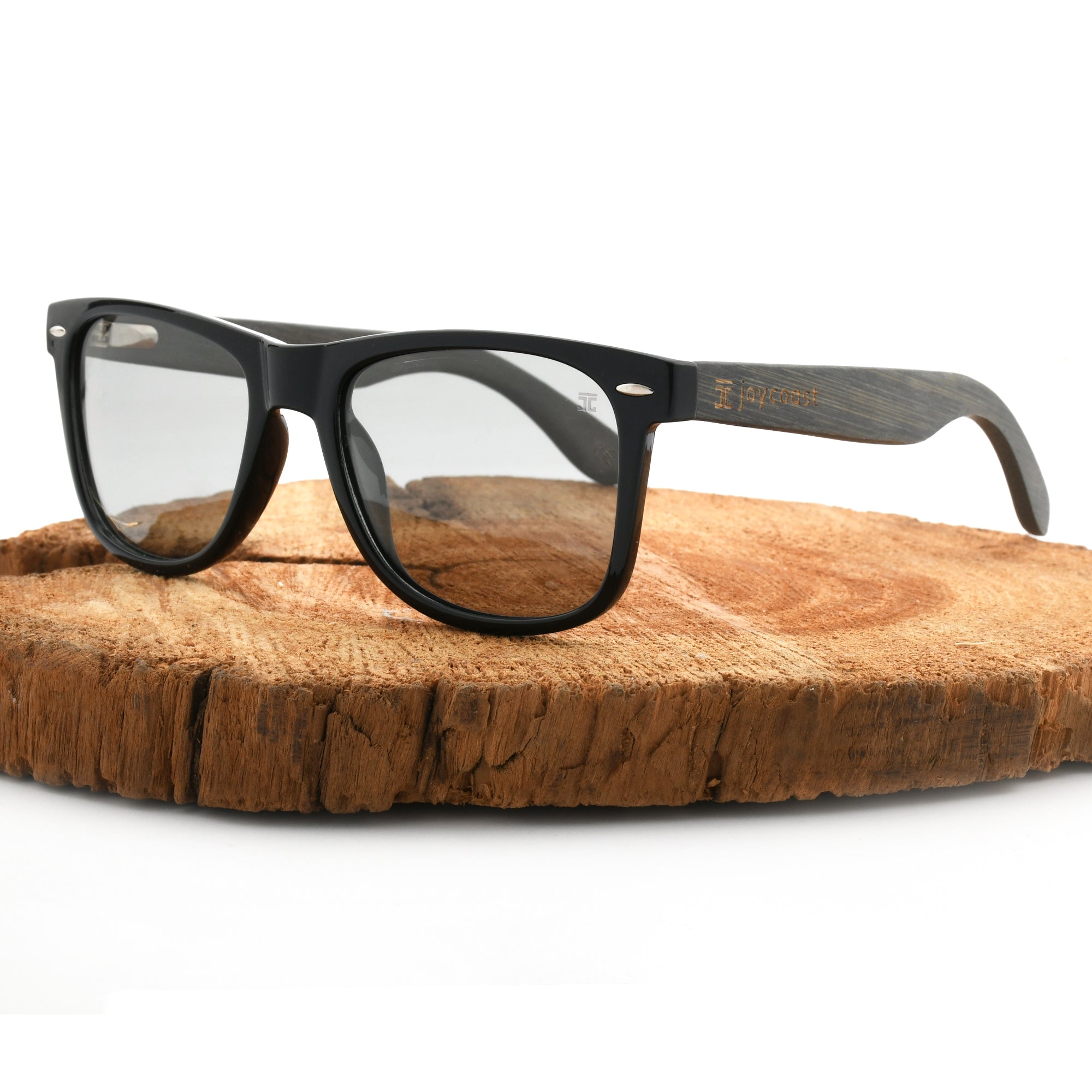 Joycoast black wooden eyeglasses with clear lenses, displayed on a natural wood slice.