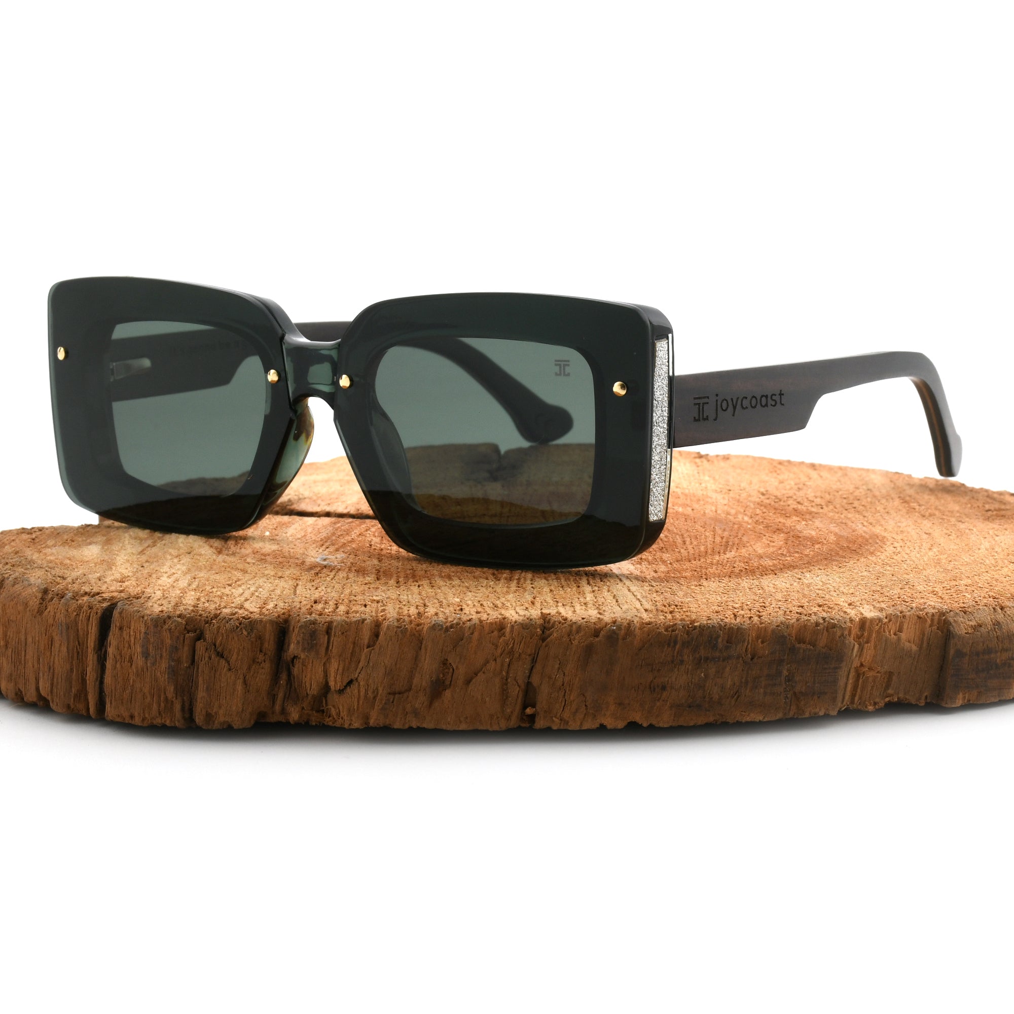 Joycoast black wooden square sunglasses with dark green lenses, displayed on a natural wood slice.