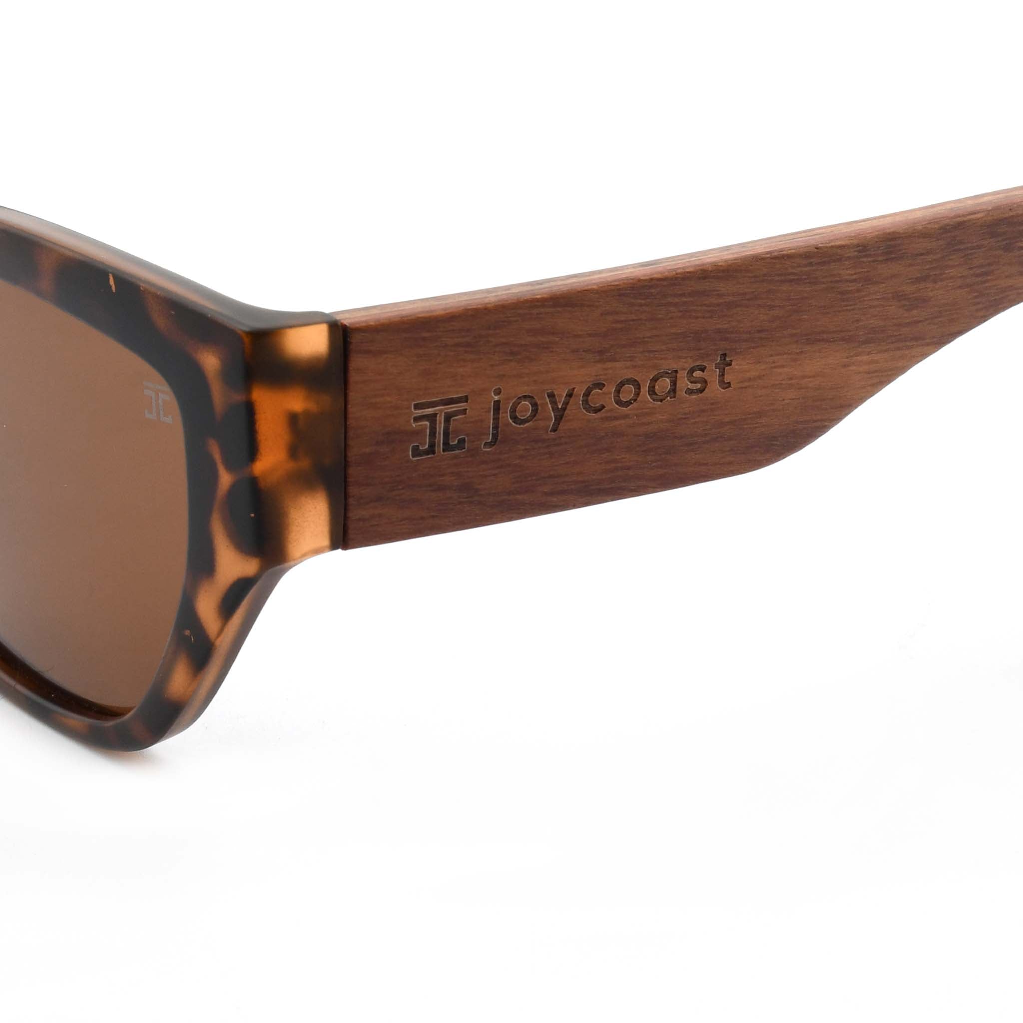 Close-up of a wooden sunglasses arm with the "Joycoast" logo and a square emblem engraved.