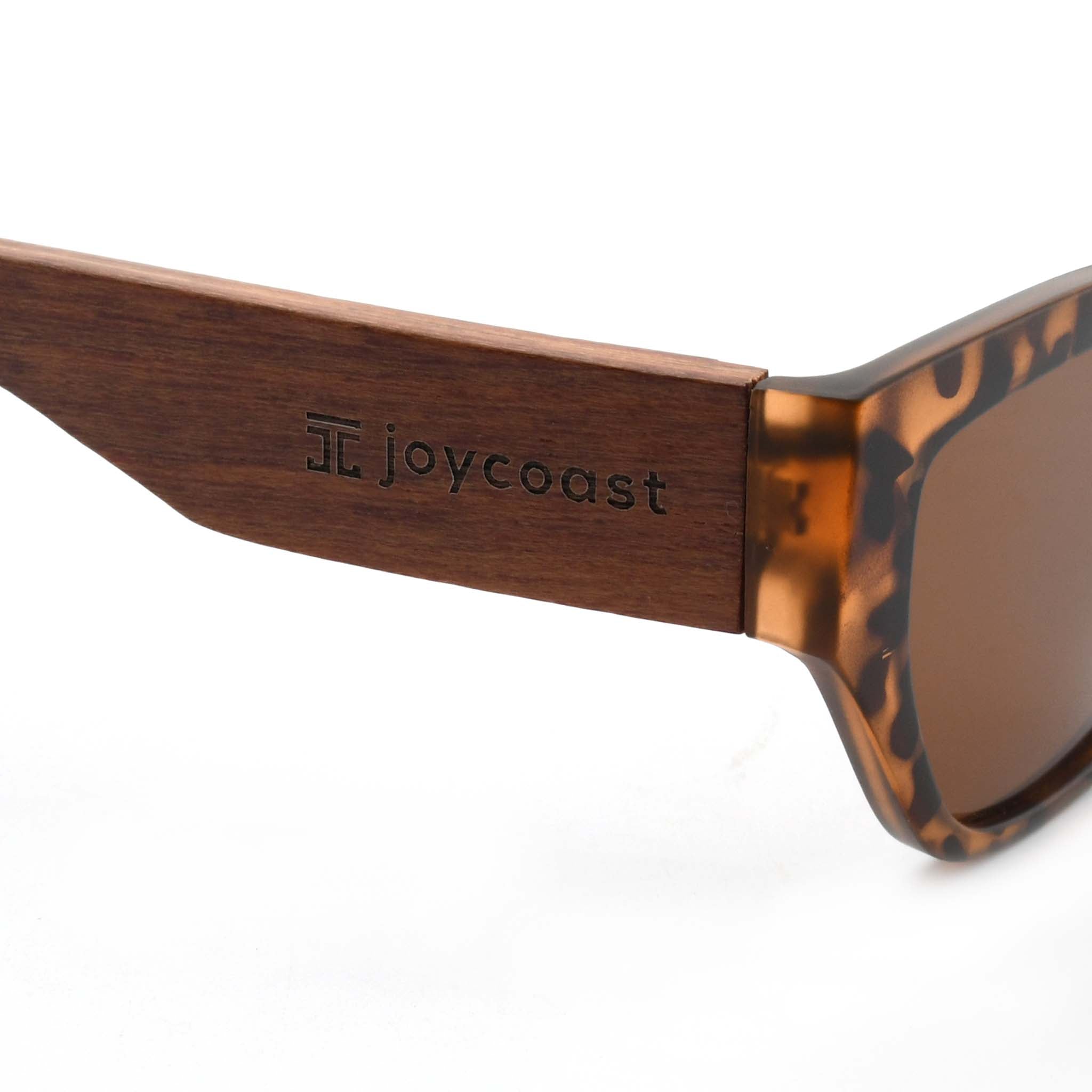 Close-up of a wooden sunglasses arm with the "Joycoast" logo and a square emblem engraved.