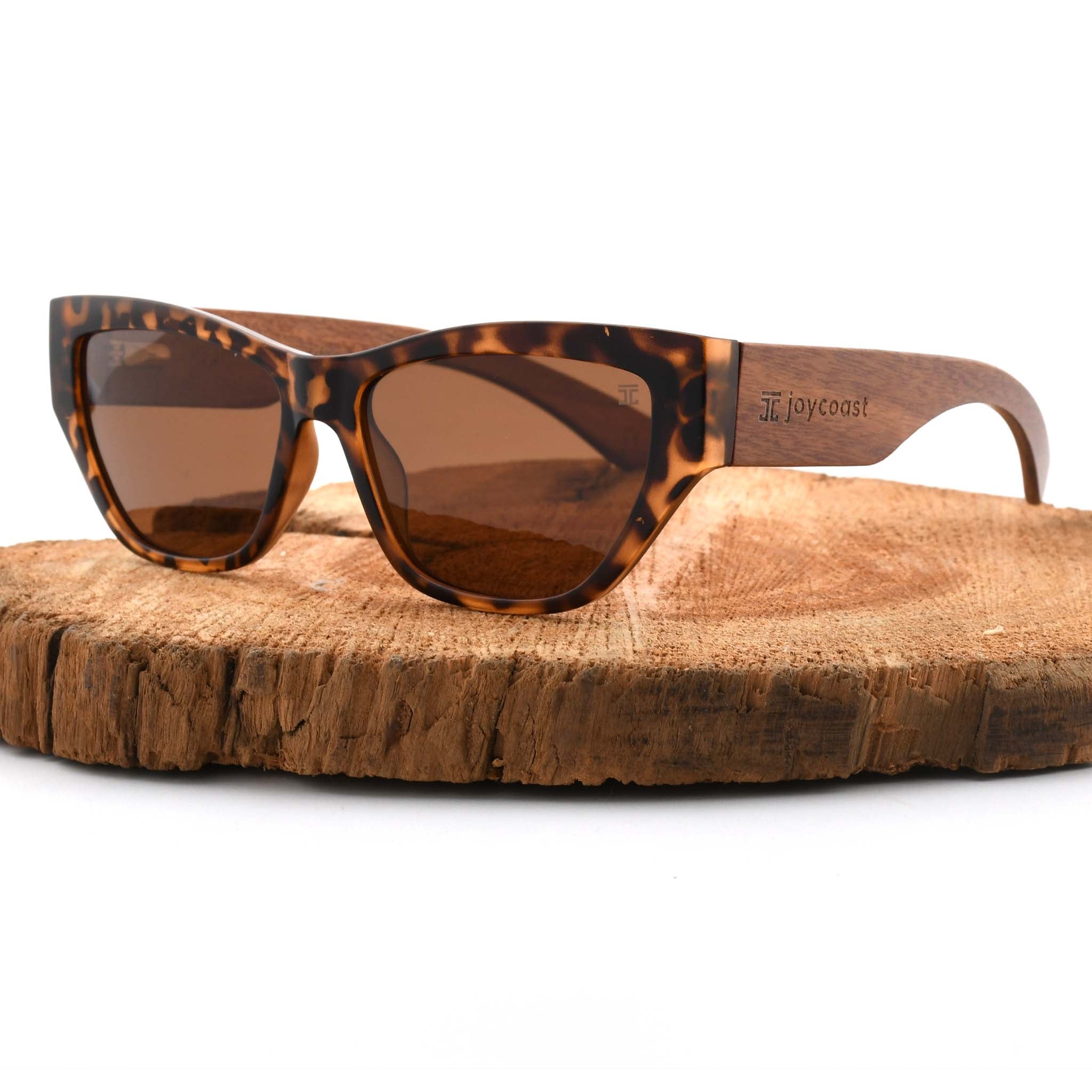 Joycoast Juniper tortoise shell sunglasses with brown lenses and wooden arms, displayed on a natural wood slice.