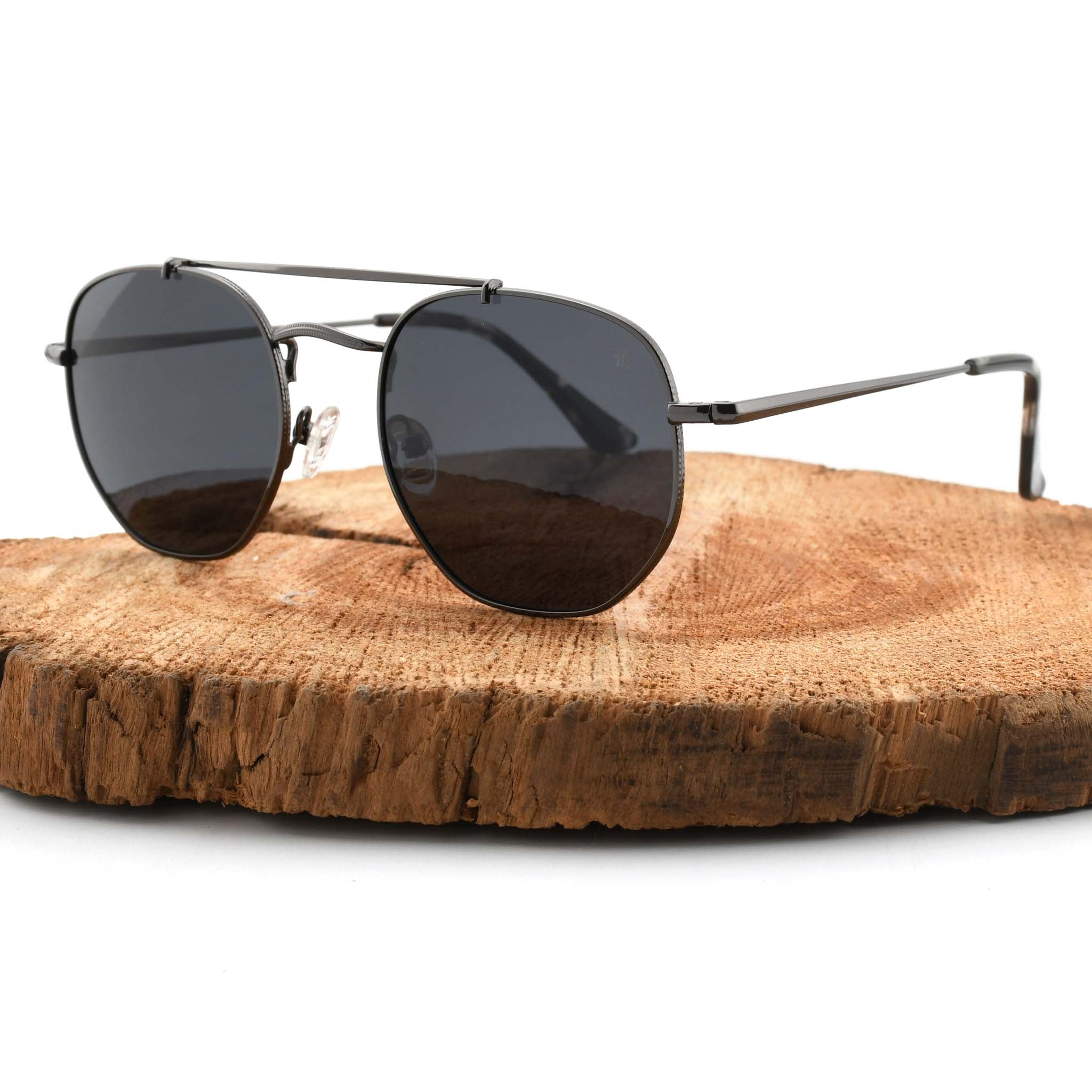 Joycoast Skyline black metal sunglasses with dark lenses, displayed on a natural wood slice.