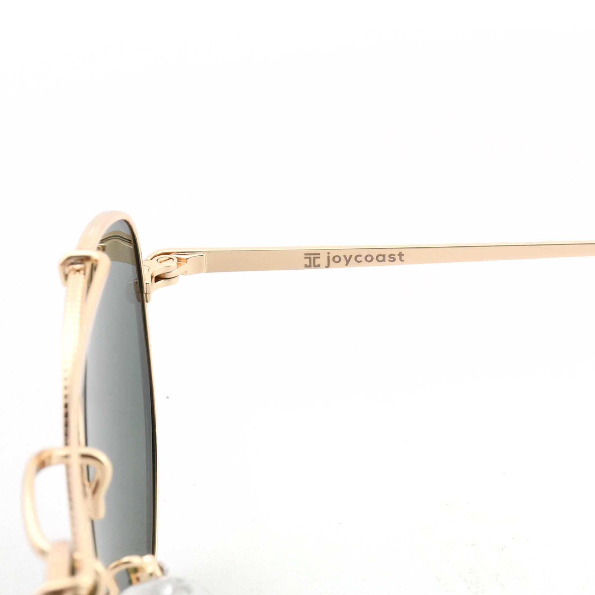 Close-up of the gold arm of Joycoast Skyline sunglasses with "Joycoast" engraved near the dark green lens.