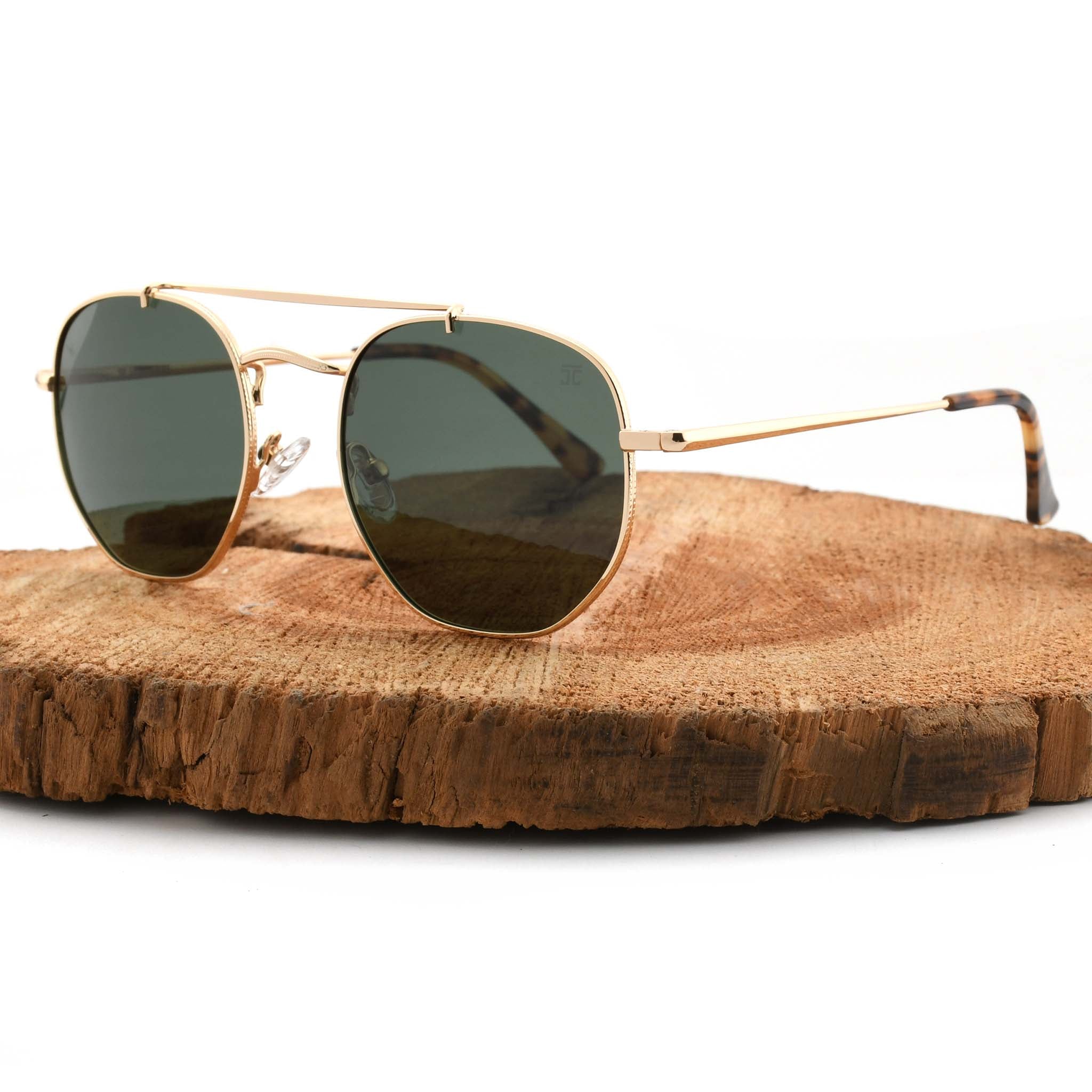 Joycoast Skyline gold metal sunglasses with dark green lenses, displayed on a natural wood slice.