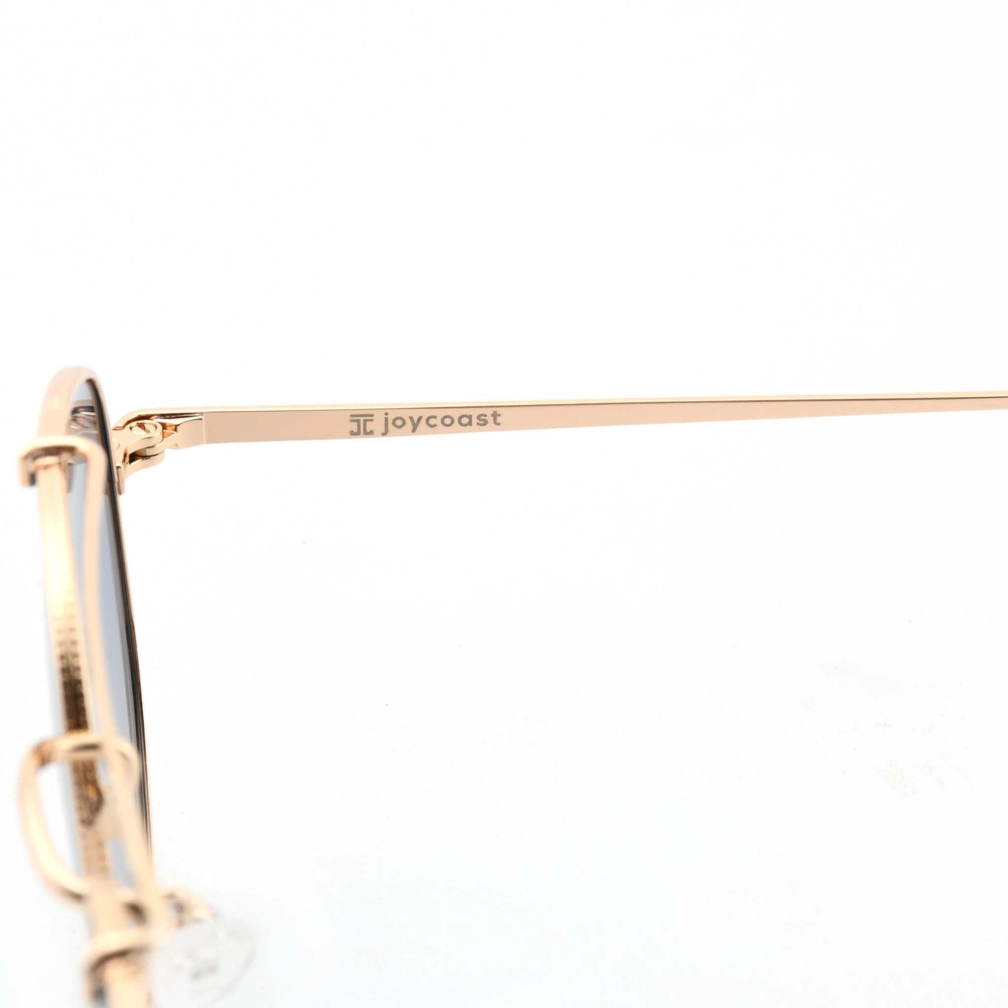 Close-up of the gold arm of Joycoast Skyline sunglasses with "Joycoast" engraved and a light blue lens visible.