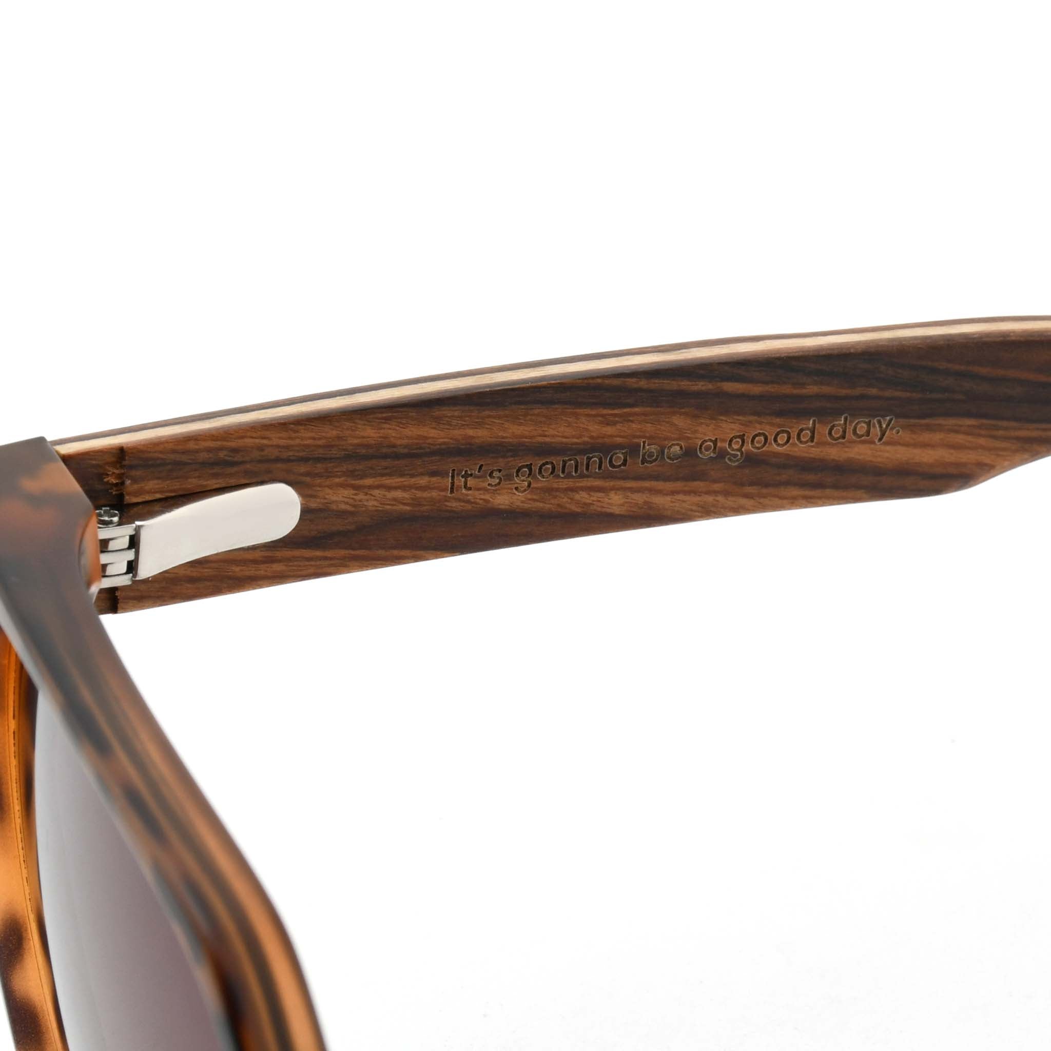 Close-up of a wooden sunglasses arm with the engraved "Joycoast" logo and slogan, "It's gonna be a good day."