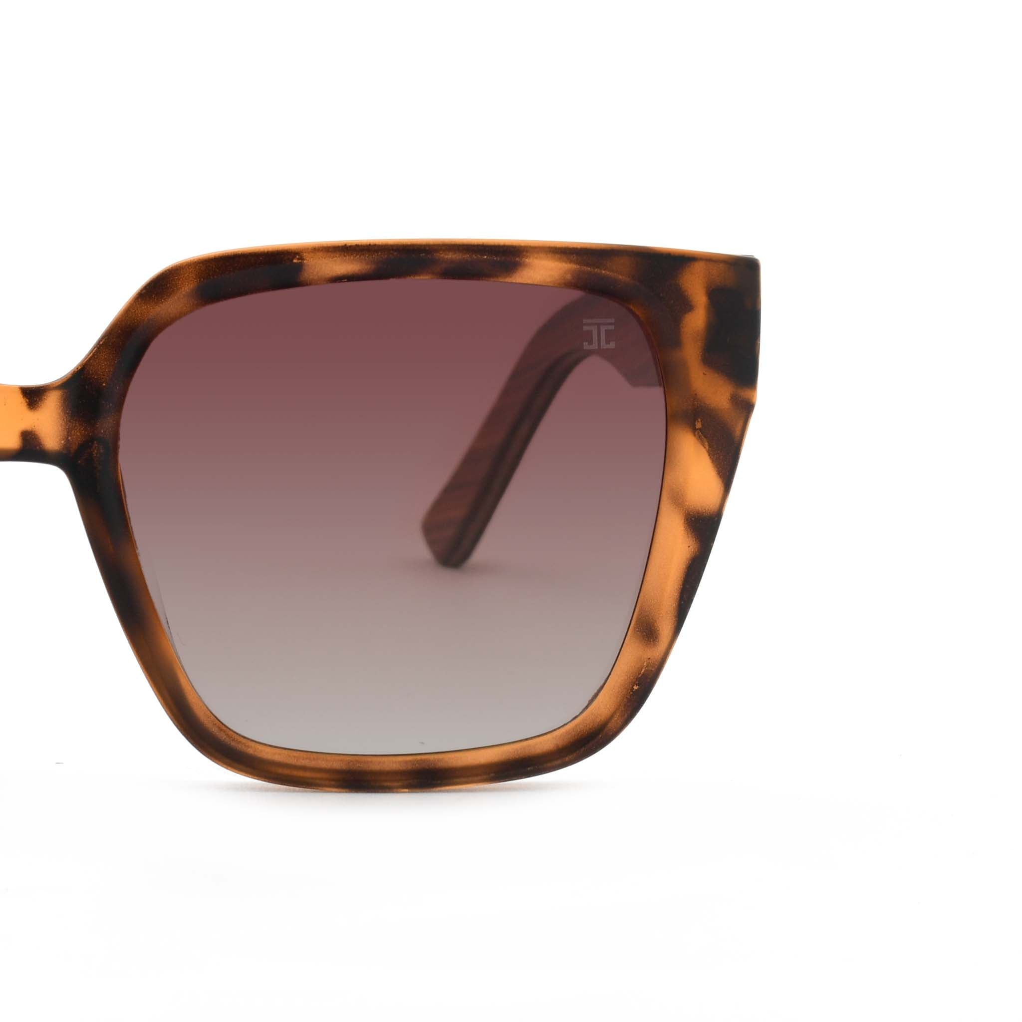 Partial view of Joycoast tortoise shell sunglasses showing the brown gradient lens and wooden frame on a white background.