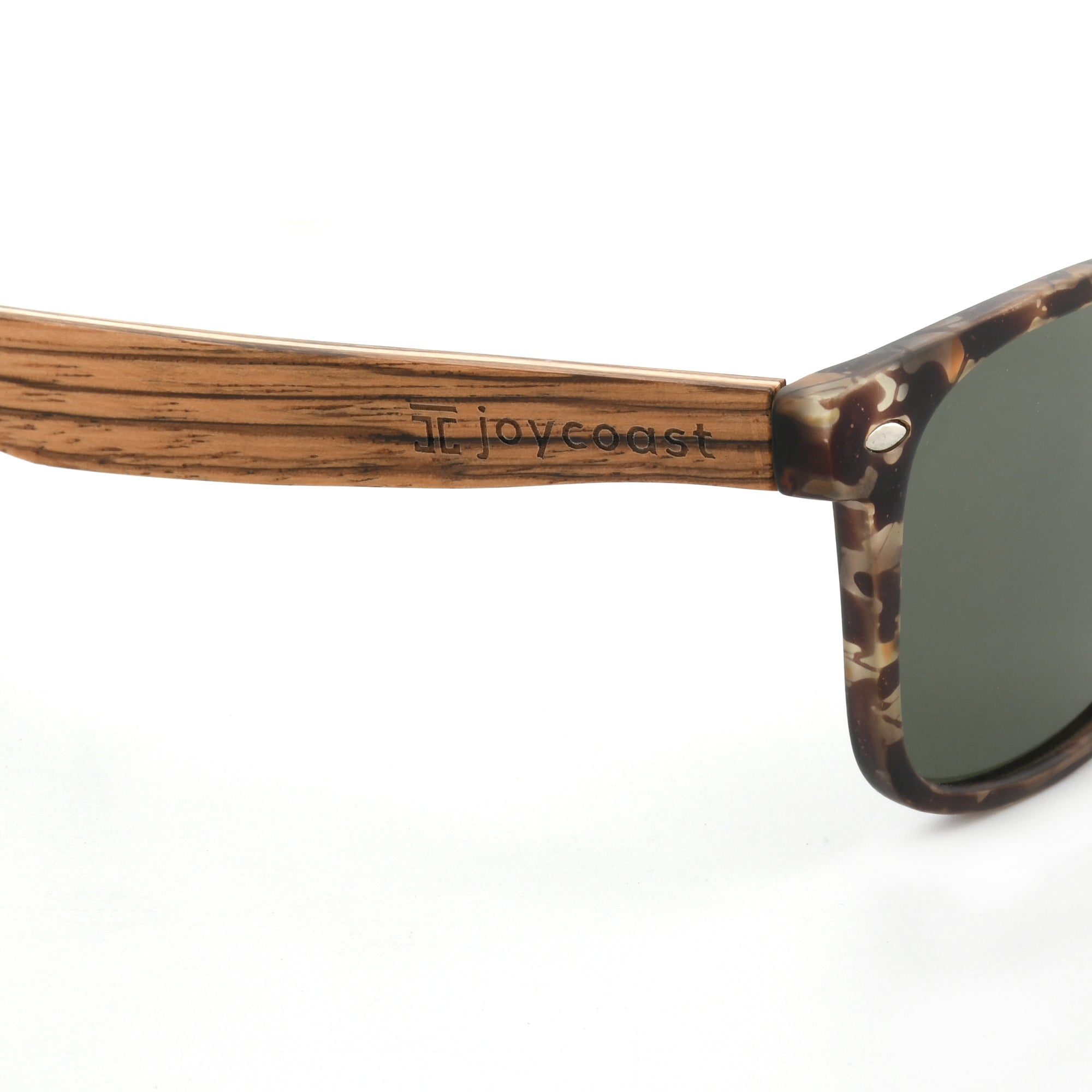 Close-up of a wooden sunglasses arm with the "Joycoast" logo engraved near the tortoise shell frame.