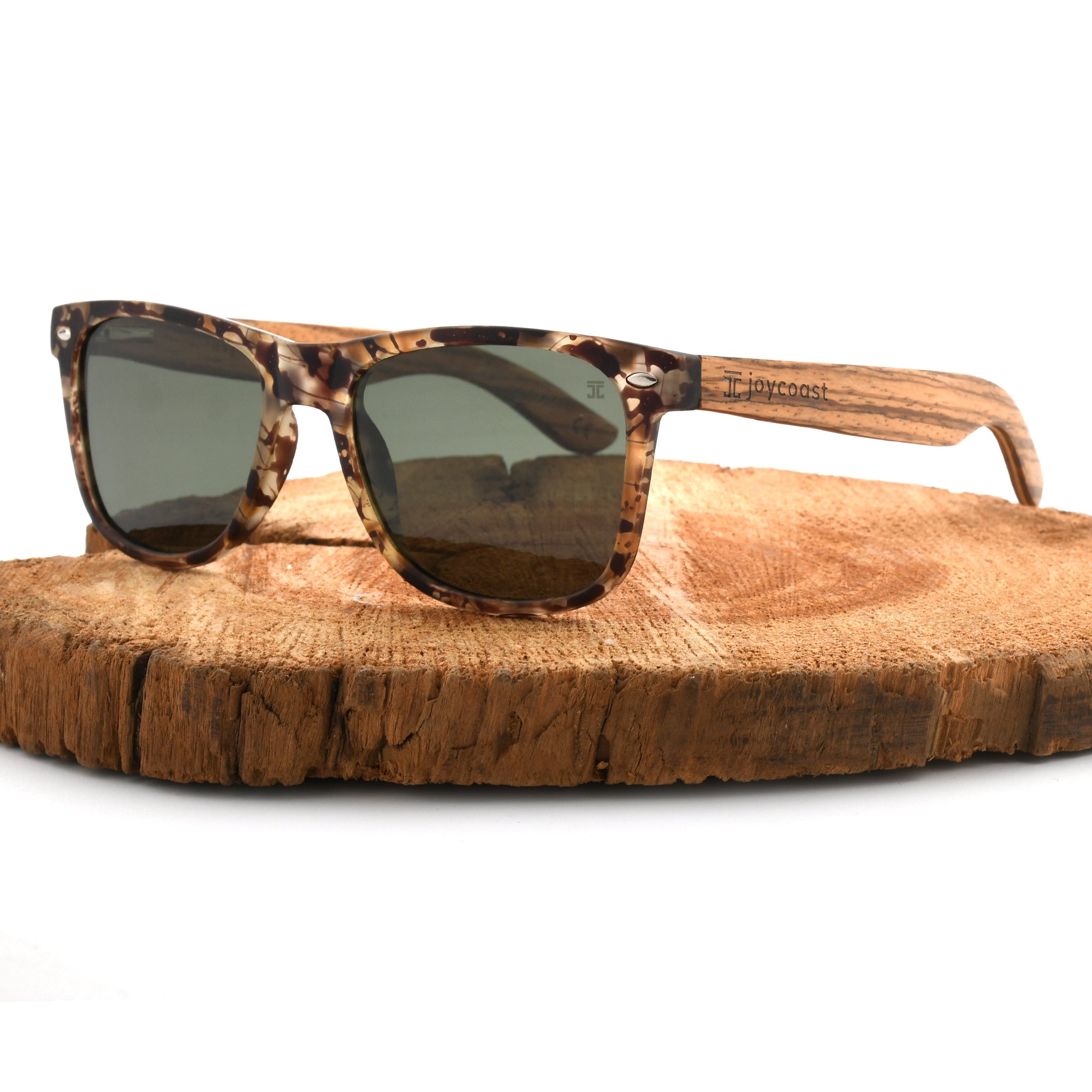 Joycoast tortoise shell wooden sunglasses with dark green lenses and a full wooden frame, displayed on a natural wood slice.