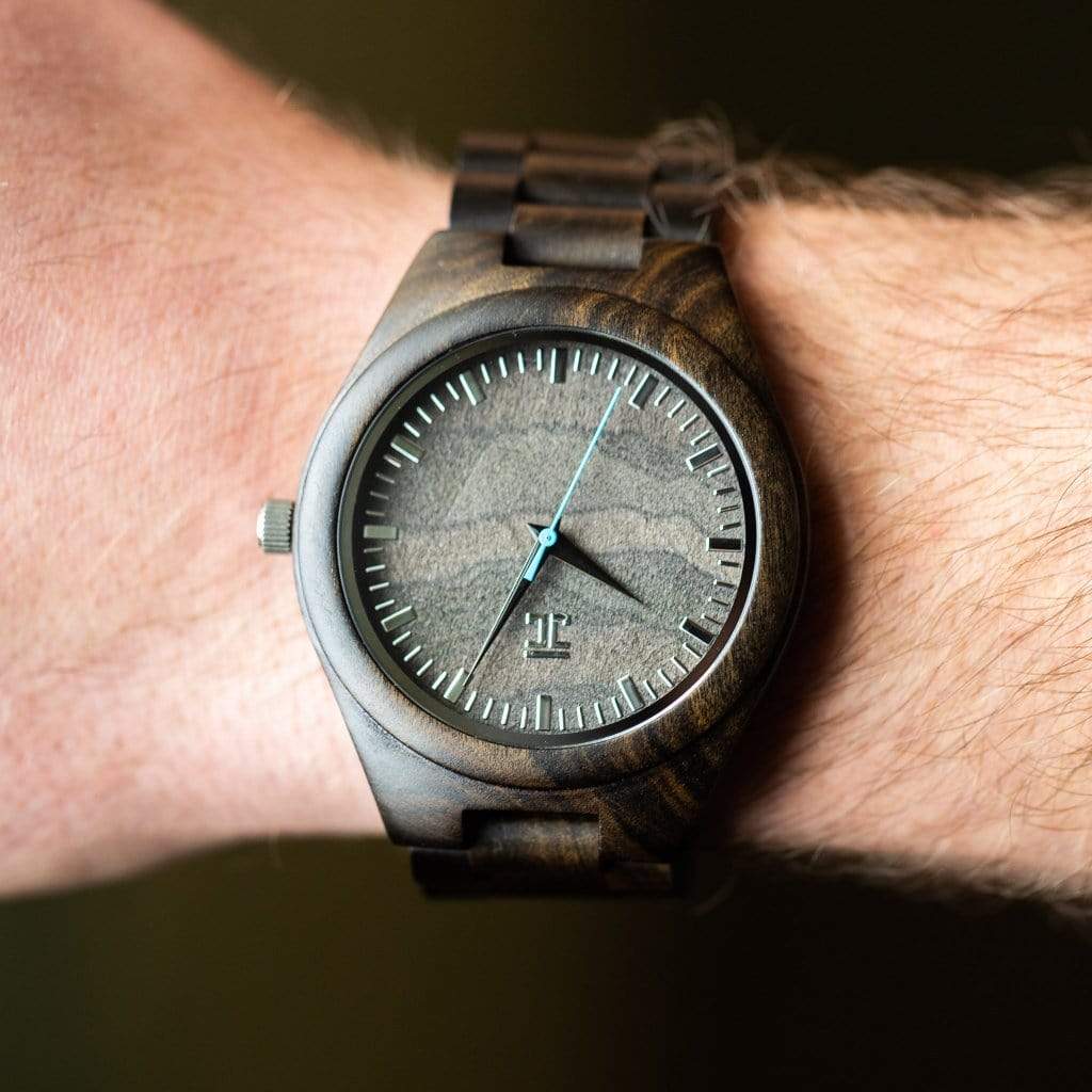 Close-up of a wrist wearing a wooden watch with light blue second hand and hour markers