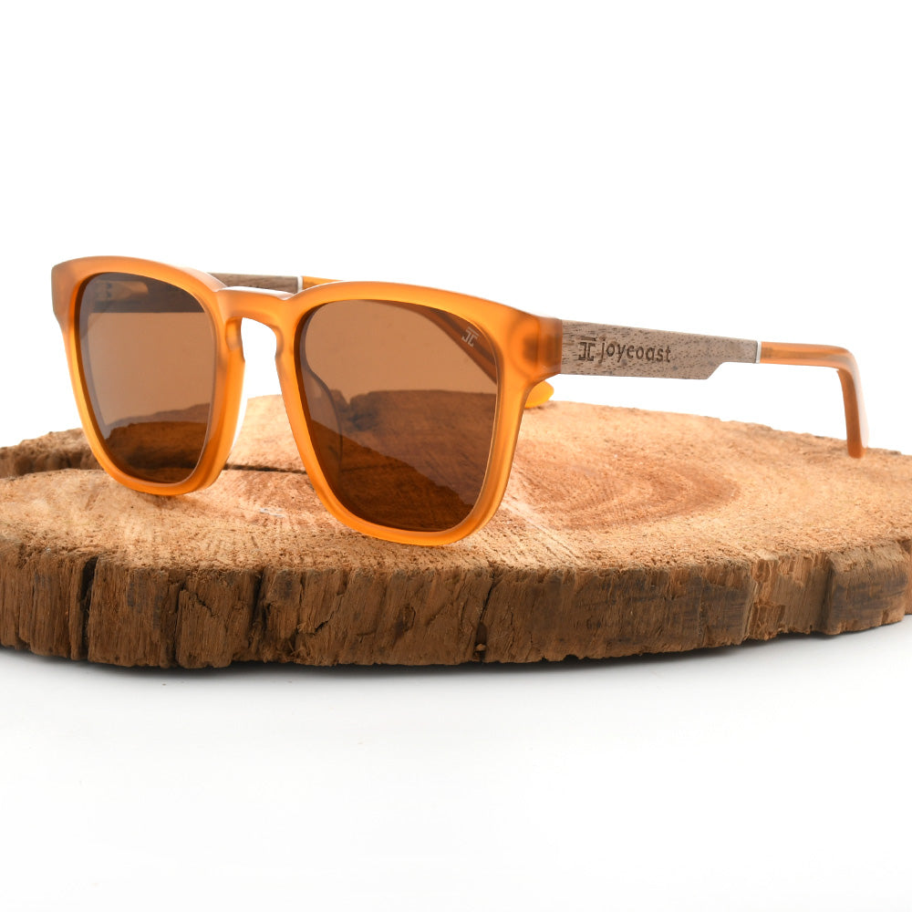Orange acetate sunglasses with brown lenses on a wooden log