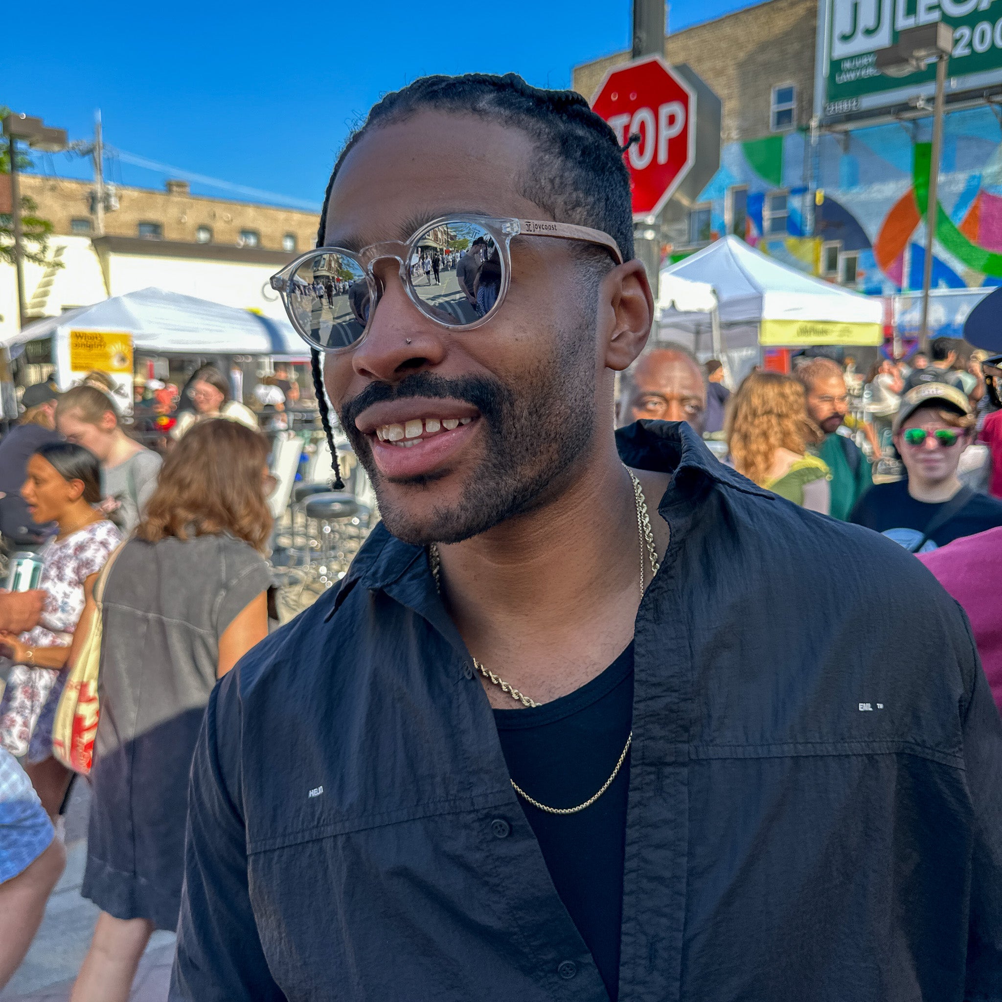 Round sunglasses on face: clear acetate frame, dark grey lenses, light wood temple arms