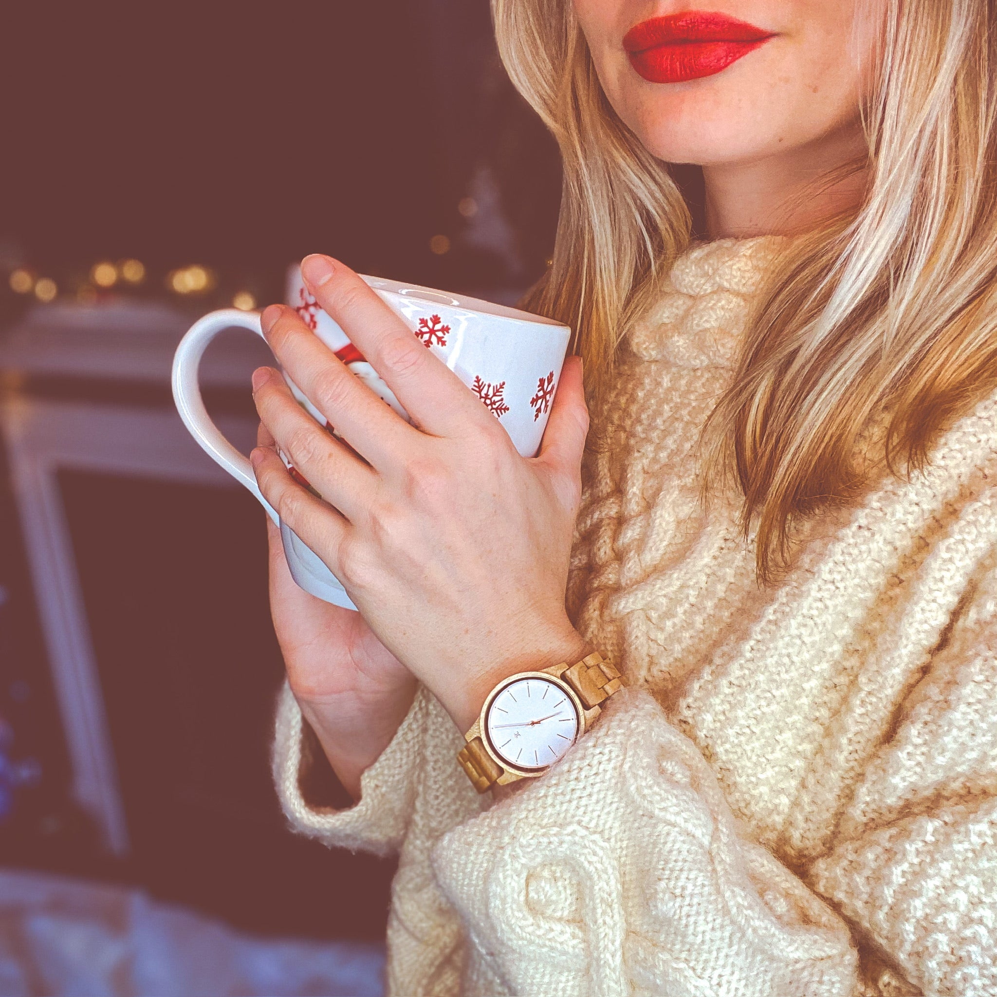 A woman in a cozy sweater holds a mug, showcasing her wooden watch, exuding warmth and comfort.