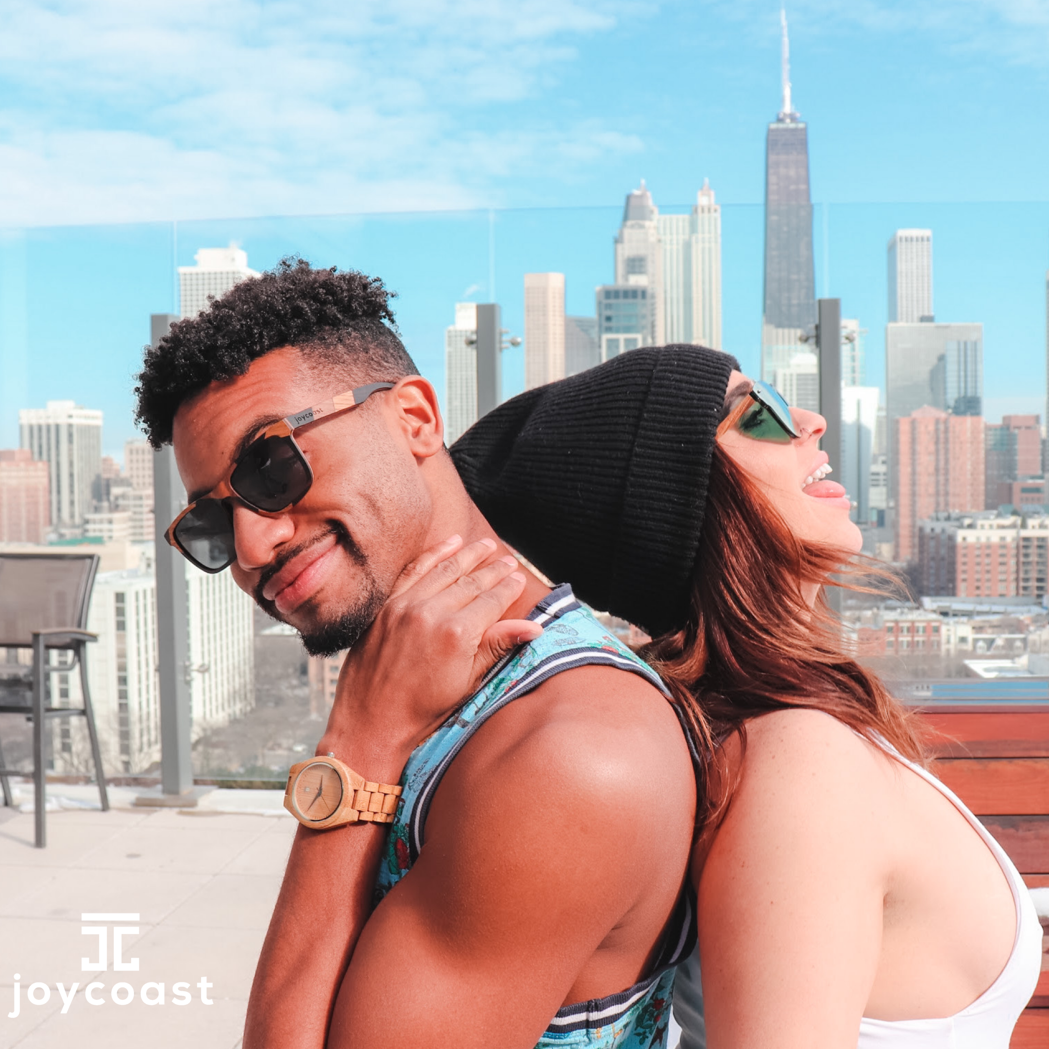 Man and woman wearing Joycoast wooden sunglasses and wooden watch with city skyline background
