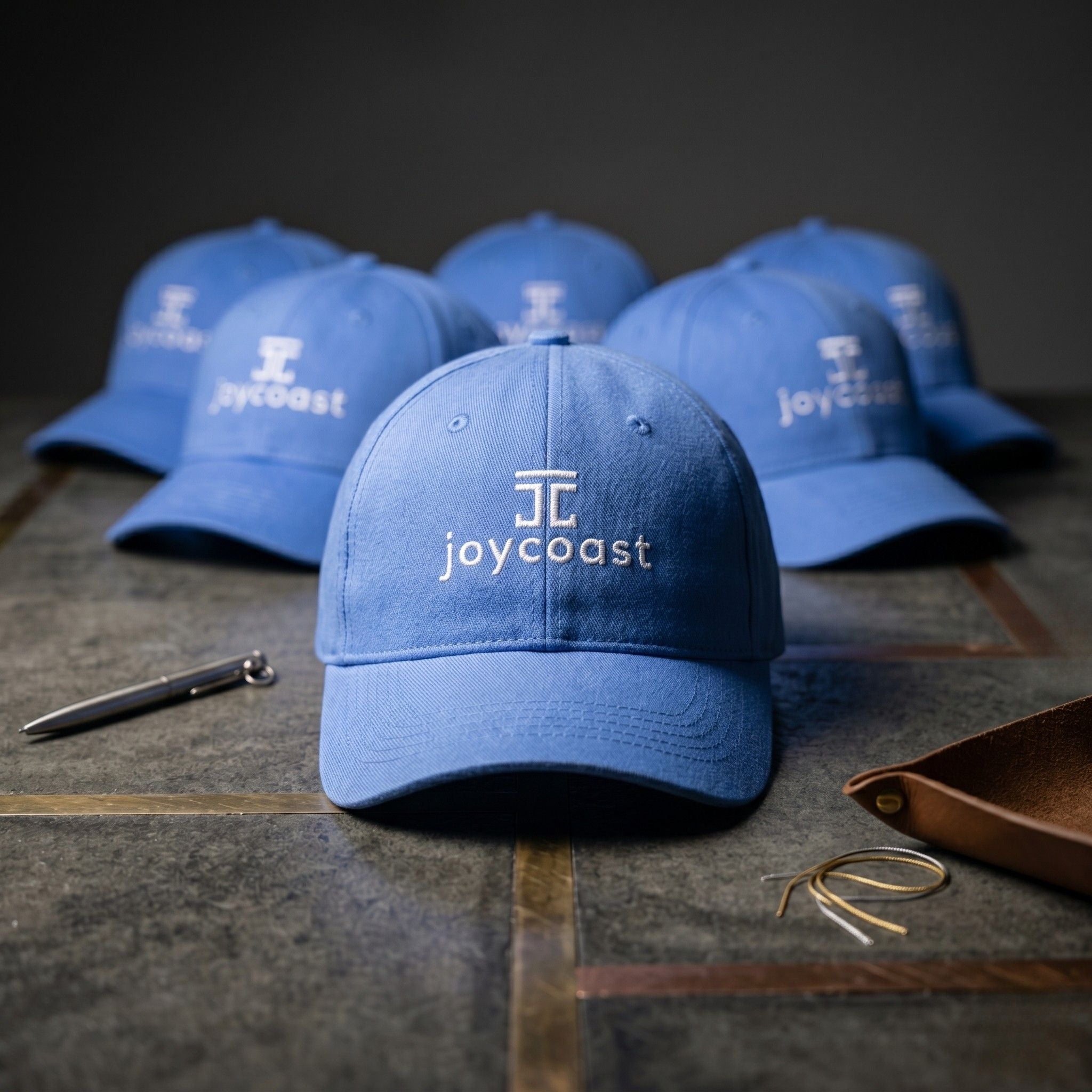 Sky blue baseball cap with Joycoast logo, with other caps behind