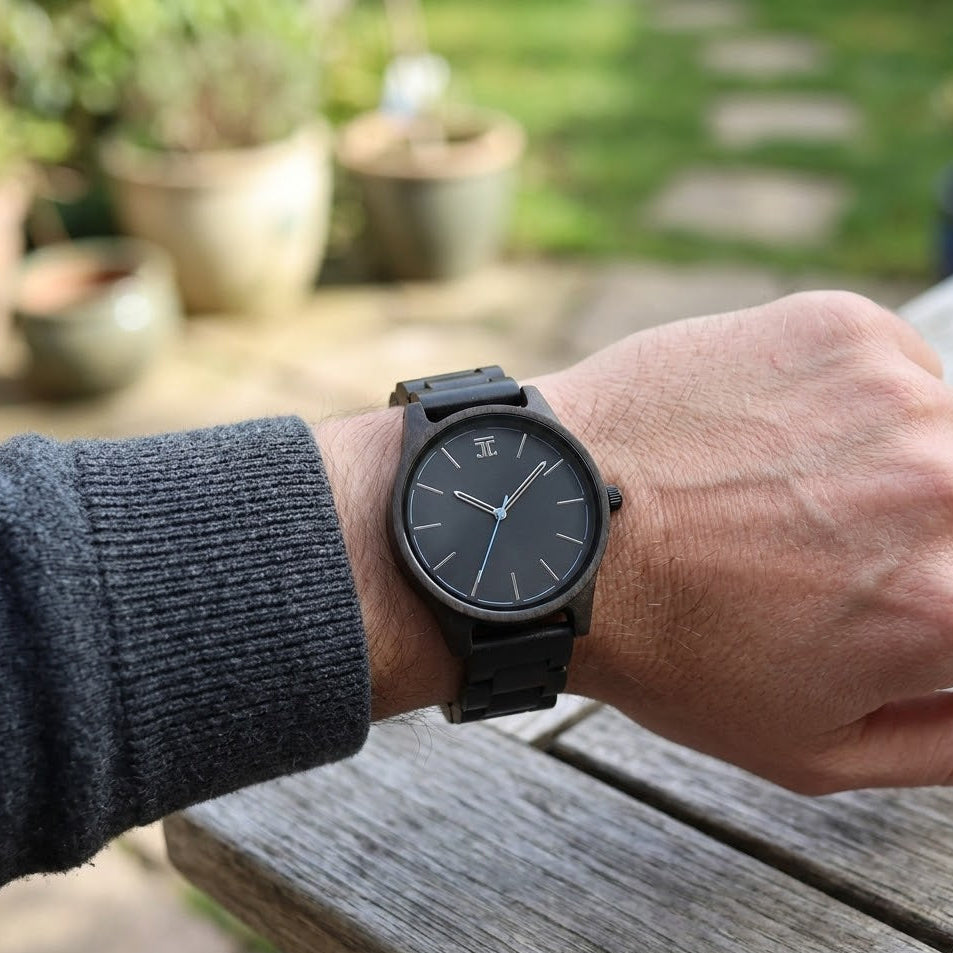 Dark wood wristwatch with black dial and stick markers, worn on a wrist