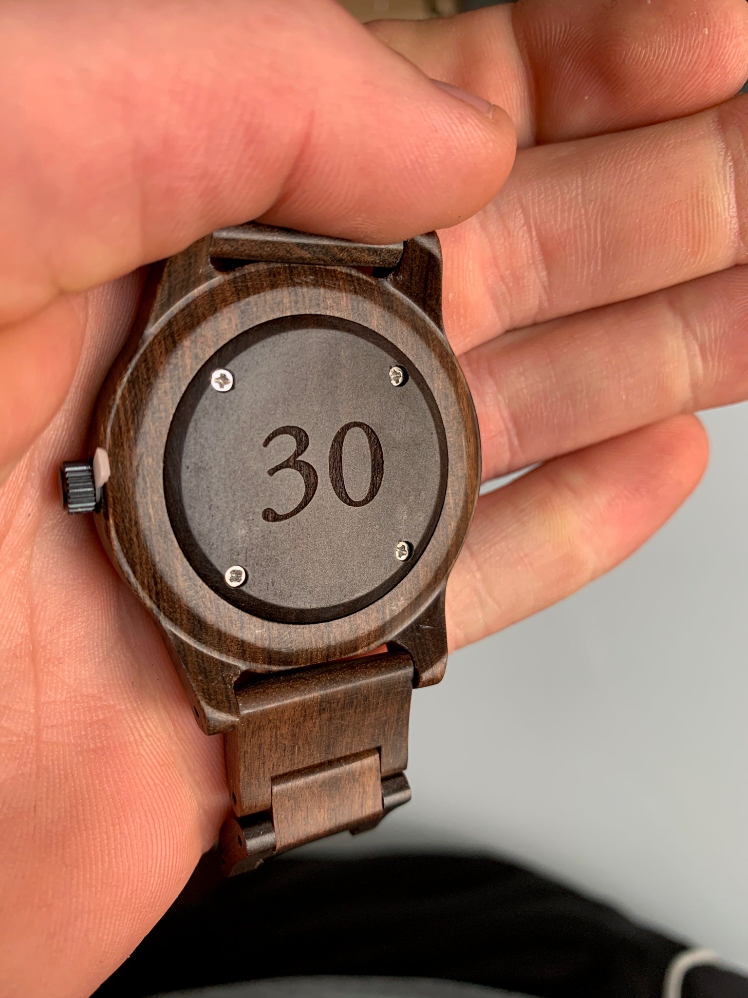 A person holding a watch prominently displaying the number 30 on its face.

