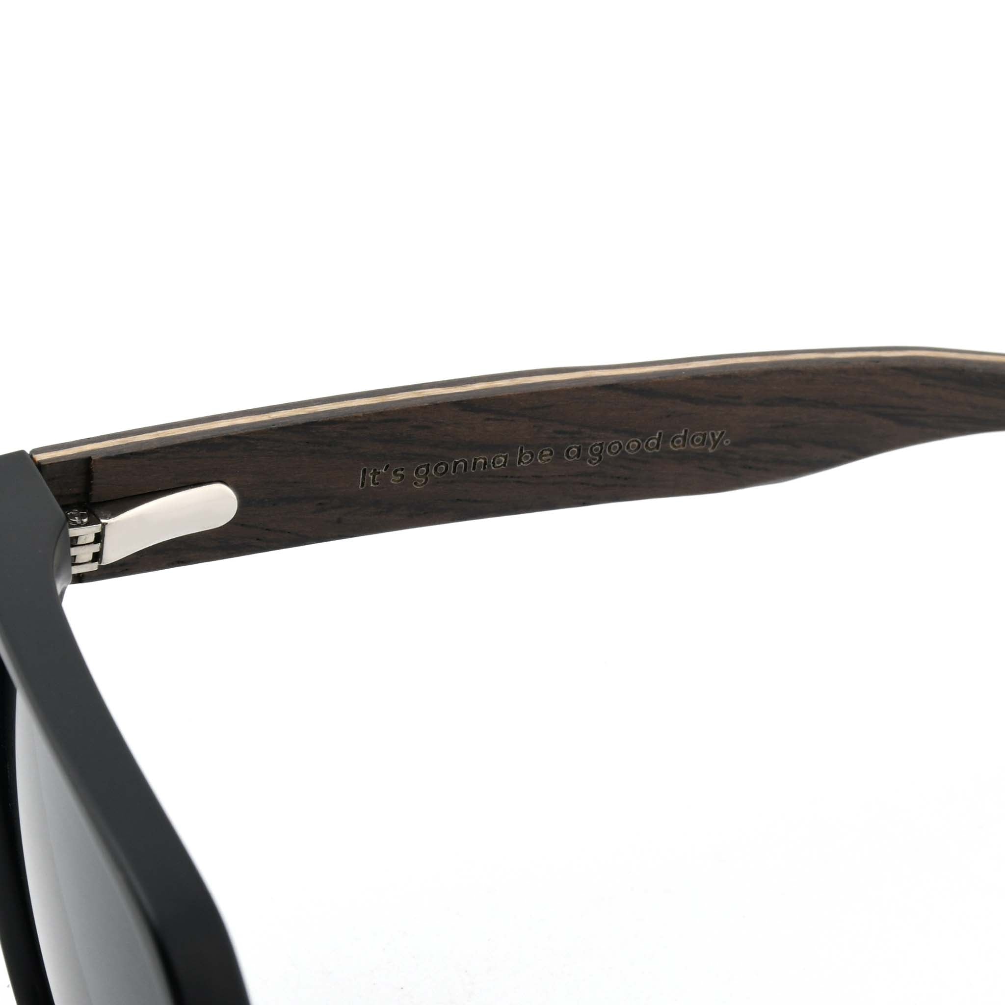 Close-up of a dark wooden sunglasses arm with the "Joycoast" logo and slogan, "It's gonna be a good day." engraved.