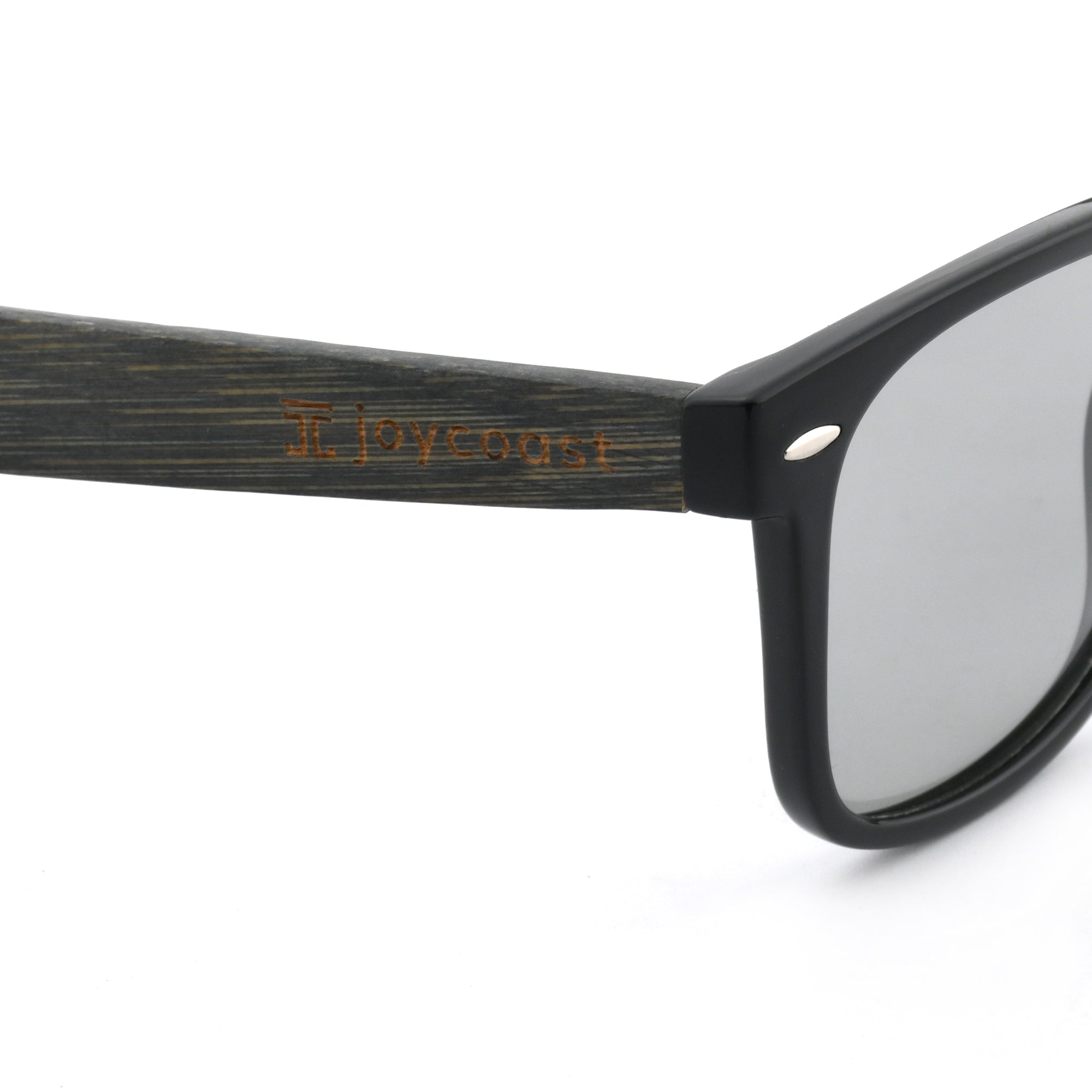 Close-up of a black wooden eyeglasses arm with the "Joycoast" logo engraved near the clear lens.