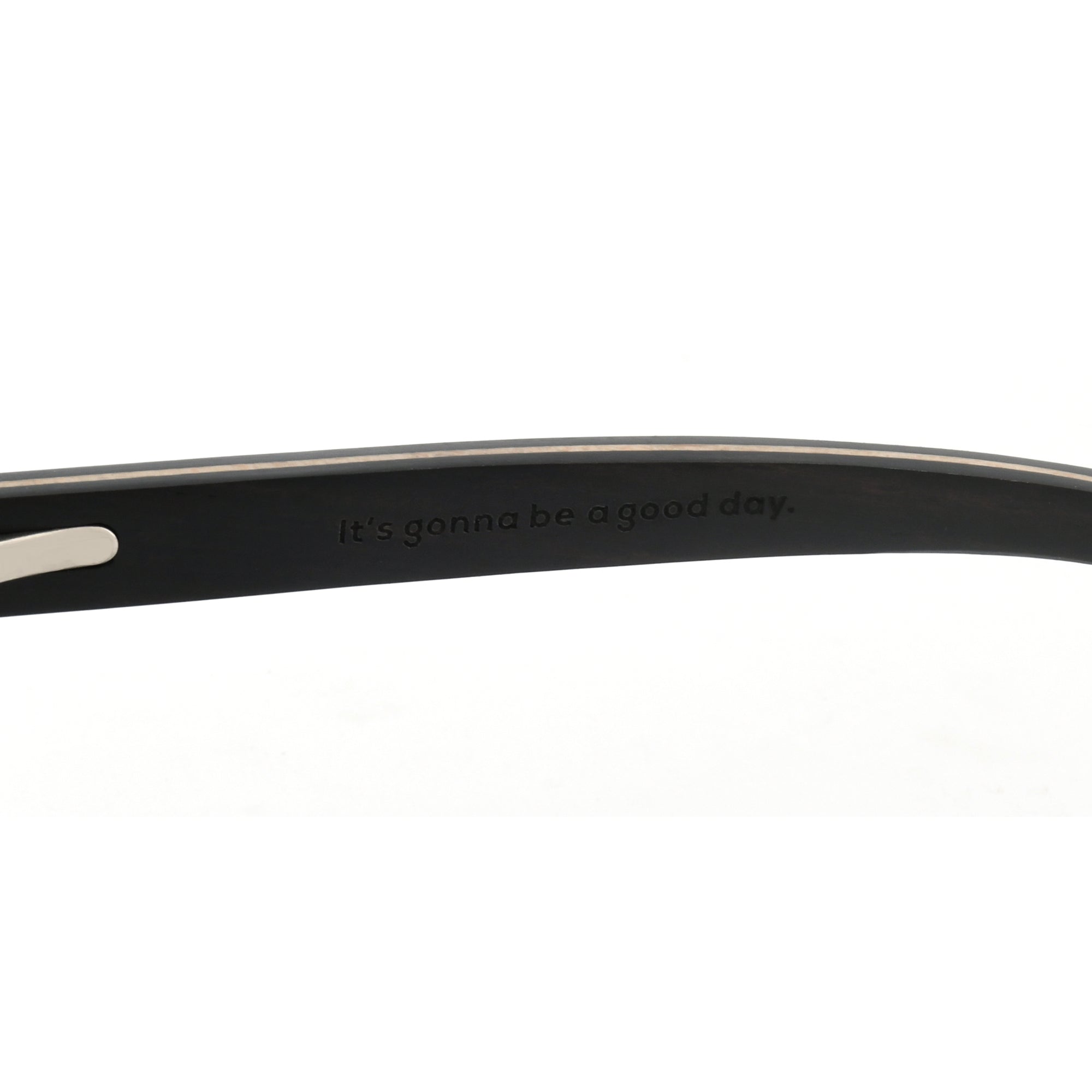 Close-up of a black wooden sunglasses arm with the Joycoast slogan, "It's gonna be a good day." engraved.