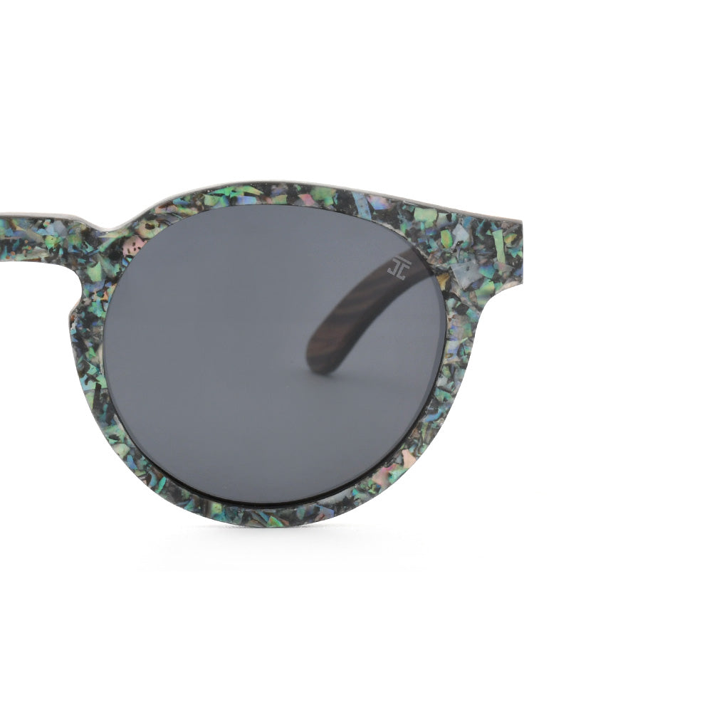 Round sunglasses close-up with abalone-pattern frame, dark gray lens.