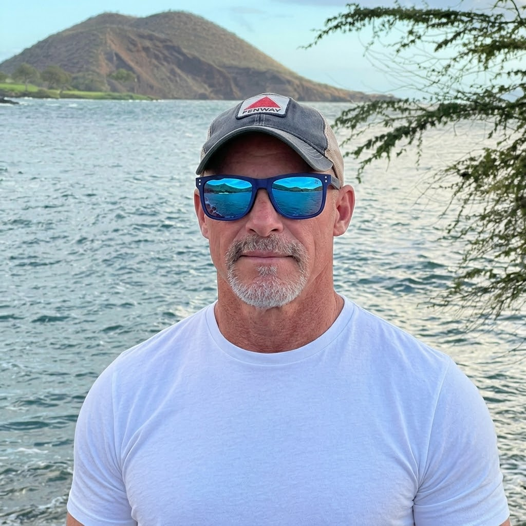 A man in sunglasses and a hat stands by the water, enjoying the sunny day.