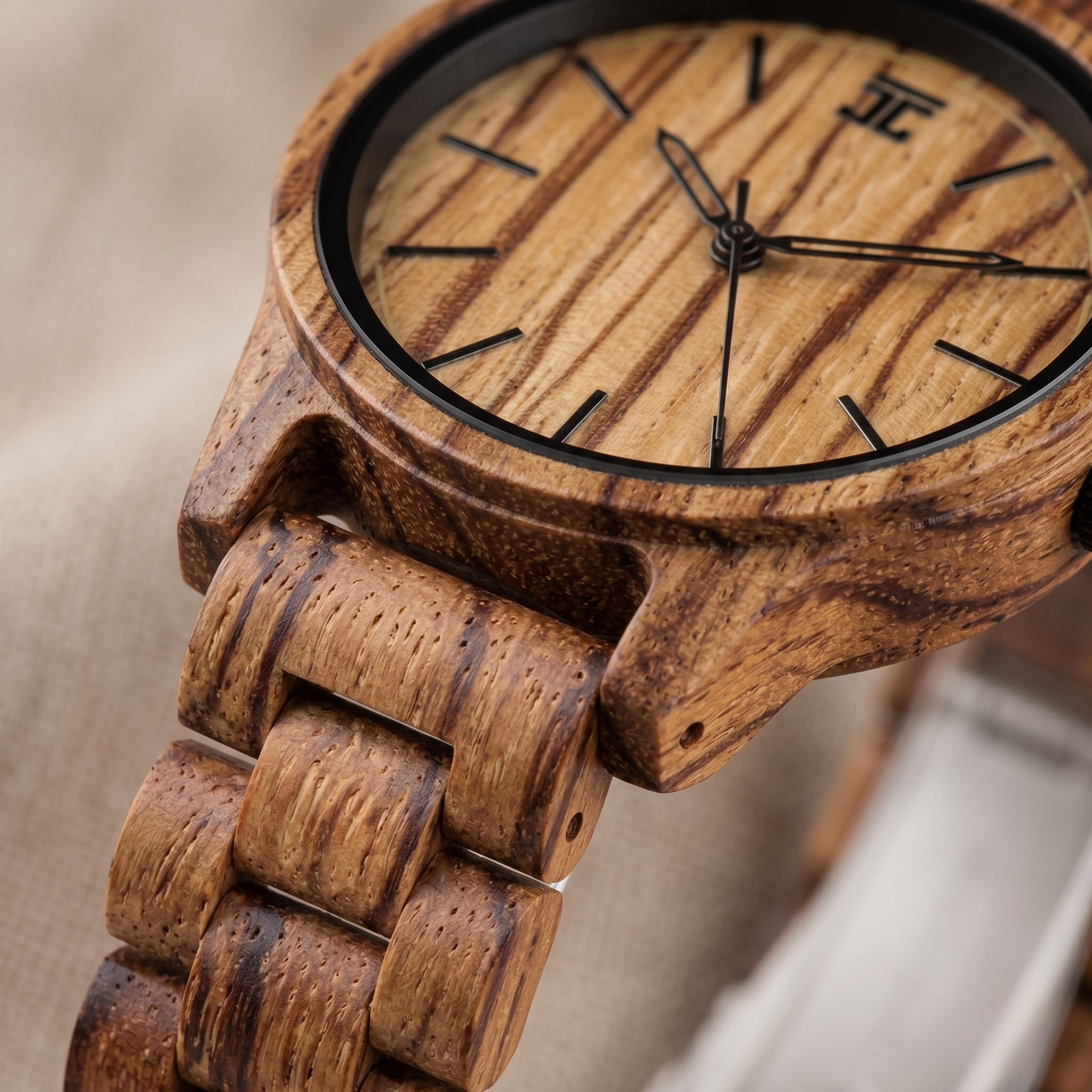 Round wooden watch face with black hour markers and wooden-link case close-up