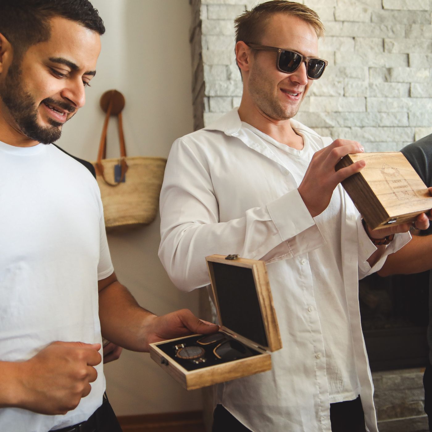 Men in white shirts and sunglasses are holding boxes, standing together in a casual outdoor setting.