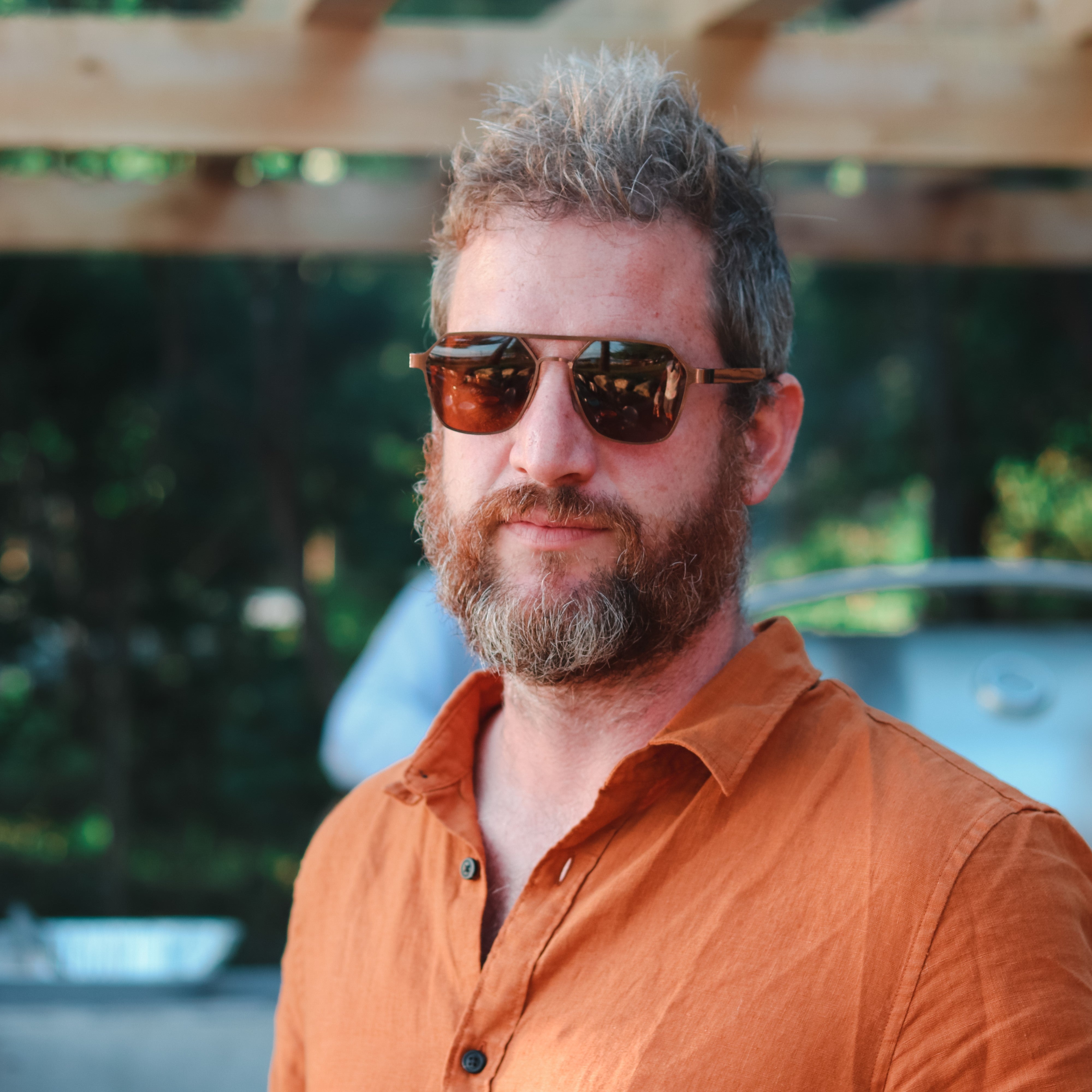 Wooden hexagon sunglasses with dark lenses and brown frame, worn by a bearded man
