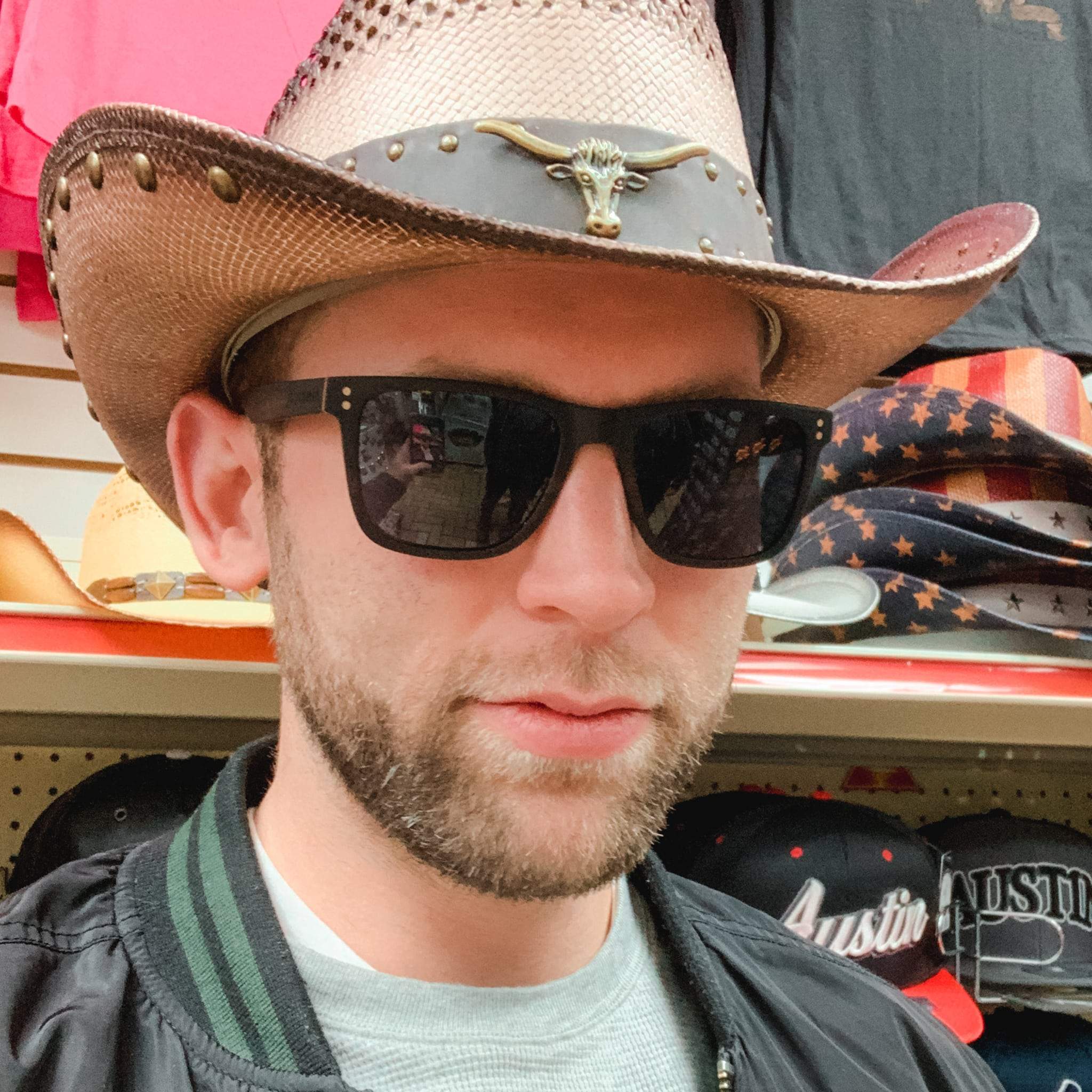 Sunglasses on a person wearing a cap, dark rectangular lenses and wood-tone frame