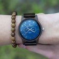 Black round chronograph watch with blue dial, Roman numerals, and dark strap